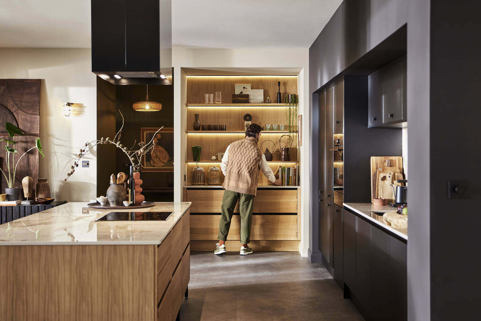 Man organising reaching for cook book in natural oak open shelves with matching wall paneling over Nordic Craft cabinetry.