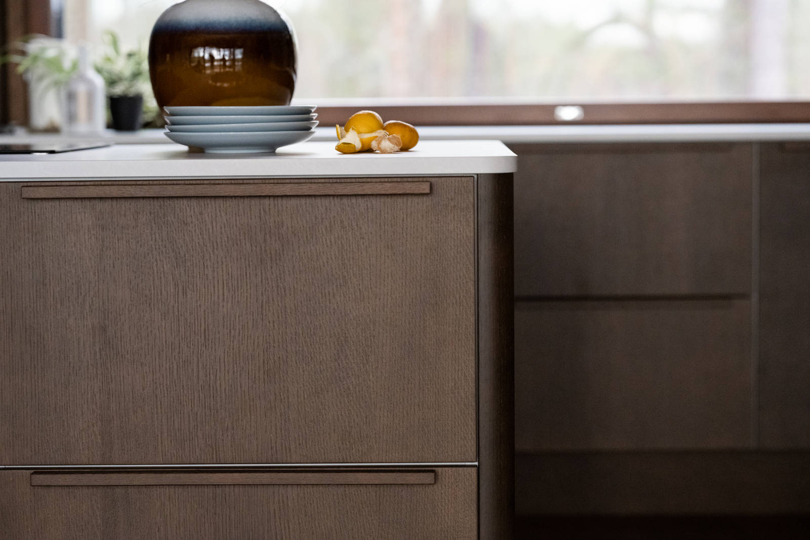 Laminaatin ja tammiviilun pyöristetyt reunat keittiösaarekkeessa, kukkalaukku työtasolla