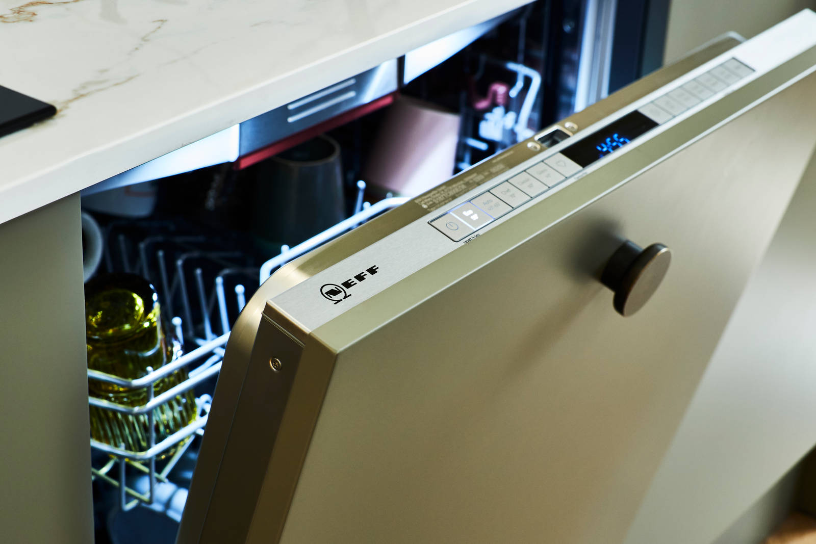 A partially open Neff dishwasher, integrated into Balmoral Green Soho cabinetry featuring a sleek white worktop and modern handle.
