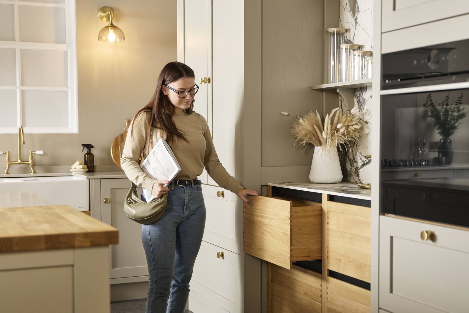 Woman holding a brochure pulling out a solid oak drawer in a showroom kitchen from Magnet, paired with neutral shade Shaker kitchen cabinets.