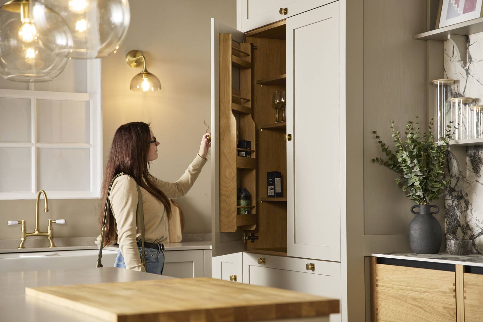 Woman in a kitchen at Magnet showroom opening larder door and looking at the oak interior.