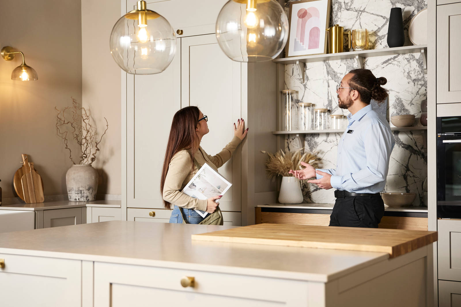 Woman holding a brochure and feeling a Shaker front with her hand while speaking to a kitchen designer in a Magnet Showroom.