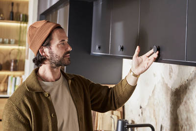 Man wearing clothes in earth tones opening a top cabinet in Hoxton Sumi Black