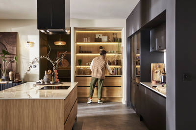 Man organising reaching for cook book in natural oak open shelves with matching wall paneling over Nordic Craft cabinetry.
