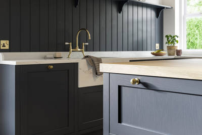 Closeup of dark blue Shaker kitchen Wardley, with painted timber finish and narrow framing. Paired with a brass kitchen tap and blue matching wall panelling.