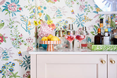 Cocktail corner in Sophie Robinsons maximalist Ludlow kitchen from Magnet, with two pink drinks poured in glasses, floral pattern wallpaper.