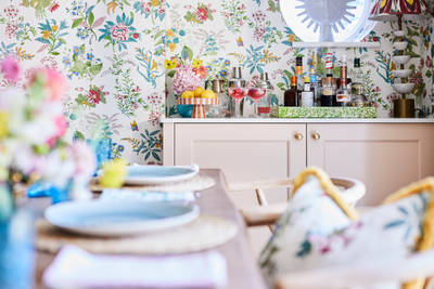 Cocktail corner in Sophie Robinsons maximalist Ludlow kitchen from Magnet, with a dining room table in foreground, floral pattern wallpaper.