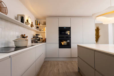 View of Yasmin Wyatt's open, light and airy neutral shade handleless Luna kitchen from Magnet, a white Corian worktop in Onyx, two AEG ovens integrated into tall cabinets.