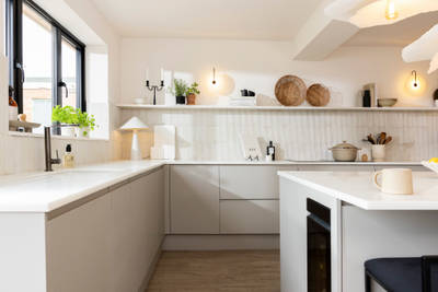 View of Yasmin Wyatt's open, light and airy neutral shade handleless Luna kitchen from Magnet, a white Corian worktop in Onyx, wine fridge integrated into kitchen island.