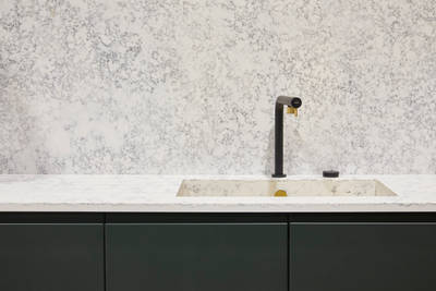 The Duxbury kitchen in rich green Arboretum, paired with white marble-effect worktops, built-in kitchen sink and a matte black and gold kitchen tap.