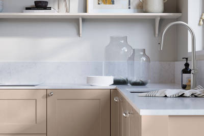 Ludlow, a traditional Shaker-style premium feel kitchen range with a visible woodgrain on its panelled doors here shown in the light shade Shell styled with steel knobs, steel tap, a white marbled worktop with matching splashback.