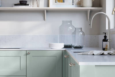 Ludlow, a traditional Shaker-style premium feel kitchen range with a visible woodgrain on its panelled doors here shown in the light blue shade Sky styled with steel knobs, steel tap, a white marbled worktop with matching splashback.