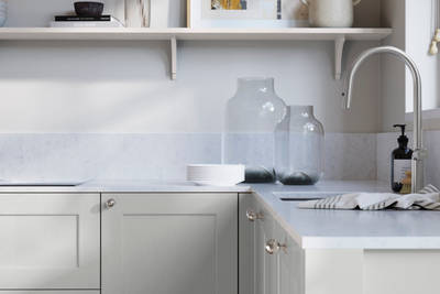 Ludlow, a traditional Shaker-style premium feel kitchen range with a visible woodgrain on its panelled doors here shown in the light shade Washed cotton styled with steel knobs, steel tap, a white marbled worktop with matching splashback.