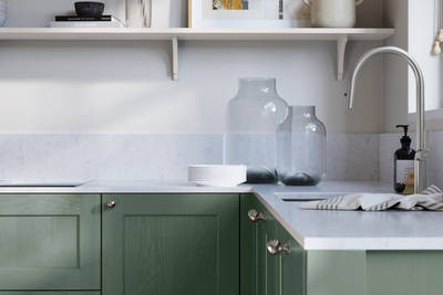 Ludlow, a traditional Shaker-style premium feel kitchen range with a visible woodgrain on its panelled doors here shown in the green shade Eucalyptus Green styled with steel knobs, steel tap, a white marbled worktop with matching splashback.