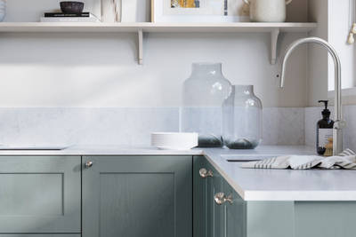 Ludlow, a traditional Shaker-style premium feel kitchen range with a visible woodgrain on its panelled doors here shown in the light blue shade Duck Egg styled with steel knobs, steel tap, a white marbled worktop with matching splashback.