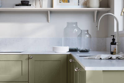 Ludlow, a traditional Shaker-style premium feel kitchen range with a visible woodgrain on its panelled doors here shown in the green shade Misty moors styled with steel knobs, steel tap, a white marbled worktop with matching splashback.