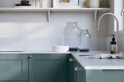 Ludlow, a traditional Shaker-style premium feel kitchen range with a visible woodgrain on its panelled doors here shown in the blue shade Morris Blue styled with steel knobs, steel tap, a white marbled worktop with matching splashback.
