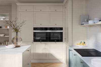 Tall Wardley Limestone cabinets with built-in ovens, steel knob handles, a white countertop on Limestone shade kitchen island and blue Duck Egg cabinets with induction hob.