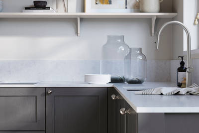 Wardley Charcoals kitchen cabinetry with steel knobs, steel tap, white marbled worktop and matching backsplash. An open shelf on the wall above cabinets with ceramics and a vase of flowers.