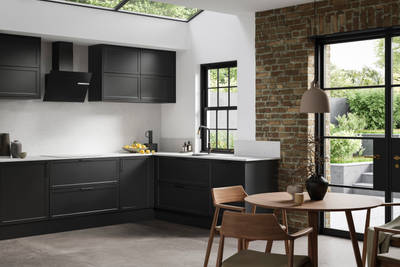 View of modern shaker kitchen Brunswick Sumi Black, with screen extractor over induction hob, black frame skylights with wood dining table and chairs in foreground, combination of white walls and sxposed brick wall.