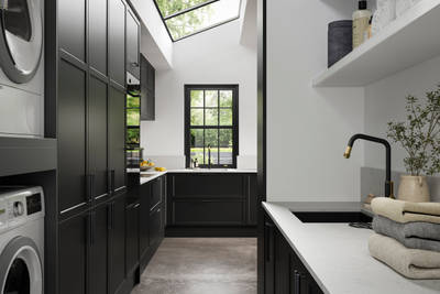 View of Modern Shaker kitchen Brunswick Sumi Black from laundry room, with integrated laundry machine and dryer, a work area with a black sink and tap,  black hex handles on cabinets and white worktop and splashback Silestone Miami Vena.