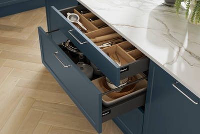 Pulled out drawers in Brunswick Voyage blue kitchen island with oak cutlery inserts, white and grey marbled worktop and light wood herringbone flooring.