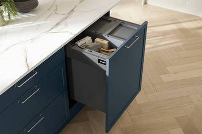 Pulled out drawer in Brunswick Voyage blue kitchen island with interior for waste recycling, white and grey marbled worktop and light wood herringbone flooring.