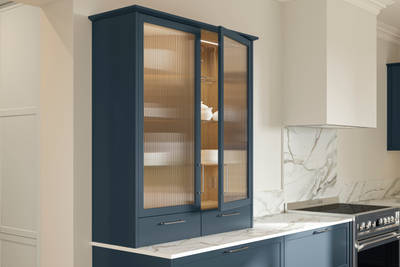 Opened vitrine cabinet with fluted glass in modern Shaker kitchen Brunswick Voyage blue, paired with a white and grey marbled worktop, matching splashback and steel handles.