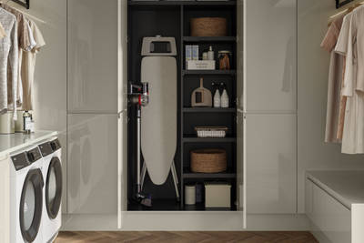 Luna Gloss Limestone utility room with tall cabinets, opened cabinets showing storage of Ironing board and laundry detergents, Amtico smouldered oak in parquet flooring.