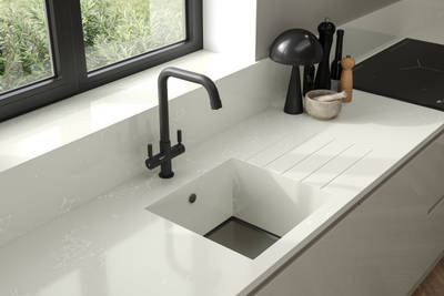 Close-up of black tap in large integrated Minerva kitchen sink bowl in Minerva worktop with matching splashback, black metal frame windows and black accessories in contemporary Luna Gloss Limestone kitchen