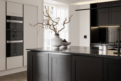Handleless frame doors Integra Wardley Sumi black kitchen with kitchen island, Integra Soho Limestone tall cabinets with integrated ovens, natural shade ceramic vase holding foliage branches.