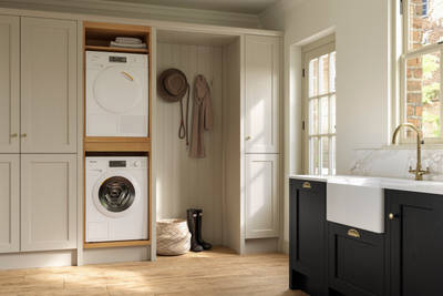 Utility room with Traditional Shaker-style tactile woodgrain Ludlow French Clay cabinets, washing machine and tumble dryer, Ludlow Sumi Black kitchen with brass accessories, Amtico oak stripwood vinyl flooring.