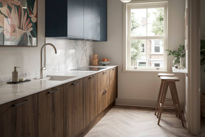 Contemporary Ascoli Mineral Blue wall cabinets over Portobello Umbra kitchen cabinets with marbled compact laminate worktop, black handles, a breakfast bar with wood bar stools, and Amtico smouldered oak herringbone flooring.