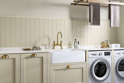 Traditional Shaker-style Ludlow Parchment and French Clay utility room with white ceramic sink, washing machine and tumble dryer with white marbled Silestone worktop and upstand, wallpanel matching the cabinetry, traditional brass tap and towels hanging on wood drying rack.