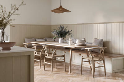 Traditional Shaker-style Ludlow Parchment bench cabinets with tactile woodgrain, a kitchen island and matching wall panel, a long wood diningroom table with matching wood chairs and ceramics set out on the table.