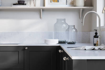 Ludlow, a traditional Shaker-style premium feel kitchen range with a visible woodgrain on its panelled doors here shown in the shade Sumi Black styled with steel knobs, steel tap, a white marbled worktop with matching splashback.