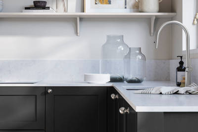 Wardley Sumi Black kitchen cabinetry with steel knobs, steel tap, white marbled worktop and matching backsplash. An open shelf on the wall above cabinets with ceramics and a vase of flowers.