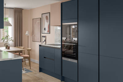 Handleless Integra Ascoli Mineral Blue, a dark blue kitchen with built-in ovens in tall cabinetry, an induction hob in white and grey marbled worktop with matching upstand.