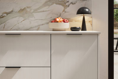 Fluted front kitchen Reed from Magnet in light shade Fresh Linen, with a marbled splashback and black handles, herringbone wood flooring.