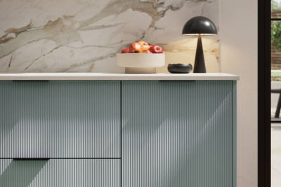 Fluted front kitchen Reed from Magnet in light blue shade Duck Egg, with a marbled splashback and black handles, herringbone wood flooring.