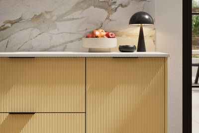 Fluted front kitchen Reed from Magnet in bright yellow shade Harvest, with a marbled splashback and black handles, herringbone wood flooring.
