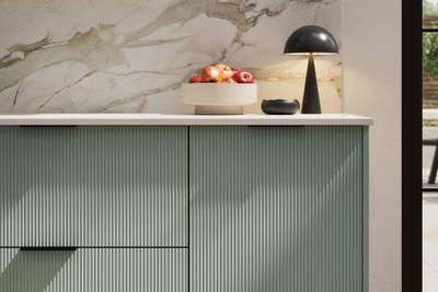 Fluted front kitchen Reed from Magnet in light green shade Eucalyptus Green, with a marbled splashback and black handles, herringbone wood flooring.