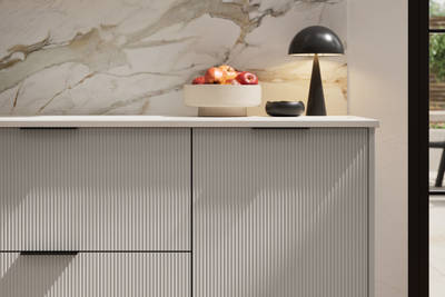 Fluted front kitchen Reed from Magnet in soft grey shade Dove Grey, with a marbled splashback and black handles, herringbone wood flooring.