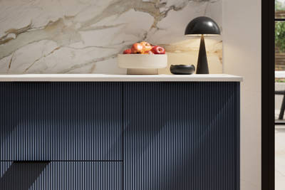 Fluted front kitchen Reed from Magnet in dark blue shade Midnight, with a marbled splashback and black handles, herringbone wood flooring.
