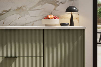 Fluted front kitchen Reed from Magnet in green shade Misty Moors, with a marbled splashback and black handles, herringbone wood flooring.