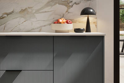 Fluted front kitchen Reed from Magnet in dark green shade Arboretum, with a marbled splashback and black handles, herringbone wood flooring.