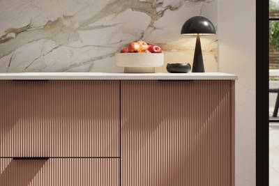 Fluted front kitchen Reed from Magnet in rich neutral green shade Baked Clay, with a marbled splashback and black handles, herringbone wood flooring.