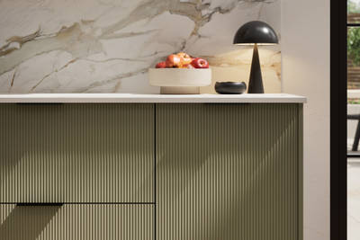 Fluted front kitchen Reed from Magnet in deep green shade Balmoral, with a marbled splashback and black handles, herringbone wood flooring.