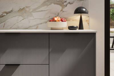Fluted front kitchen Reed from Magnet in dark grey shade Charcoals, with a marbled splashback and black handles, herringbone wood flooring.