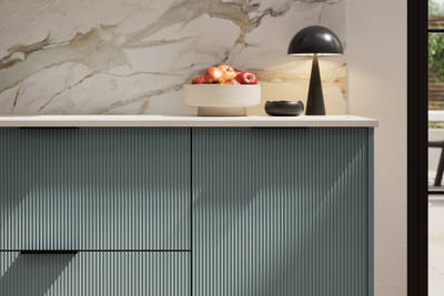 Fluted front kitchen Reed from Magnet in blue shade Coastland, with a marbled splashback and black handles, herringbone wood flooring.